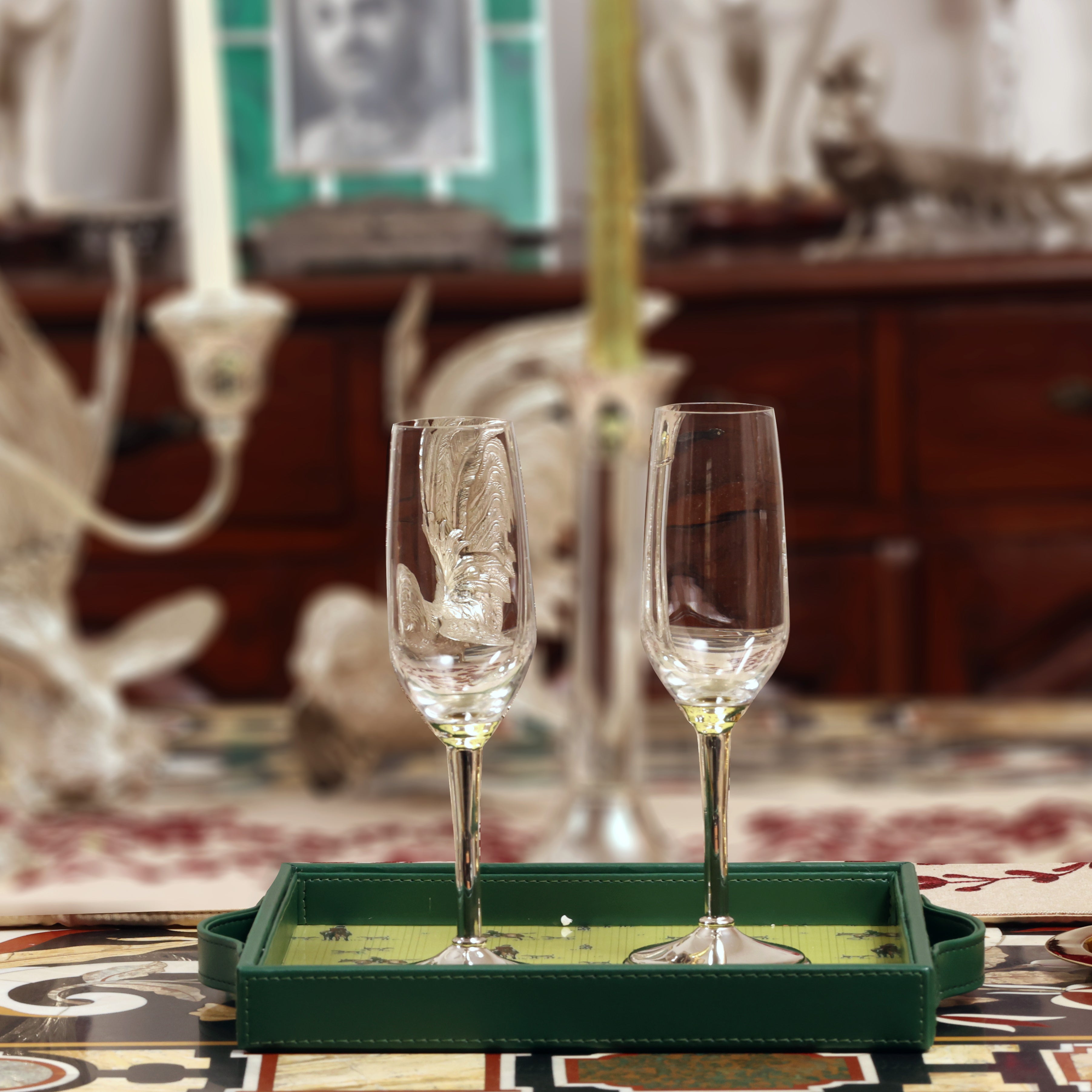 Two champagne flutes on a green tray with a decorative background