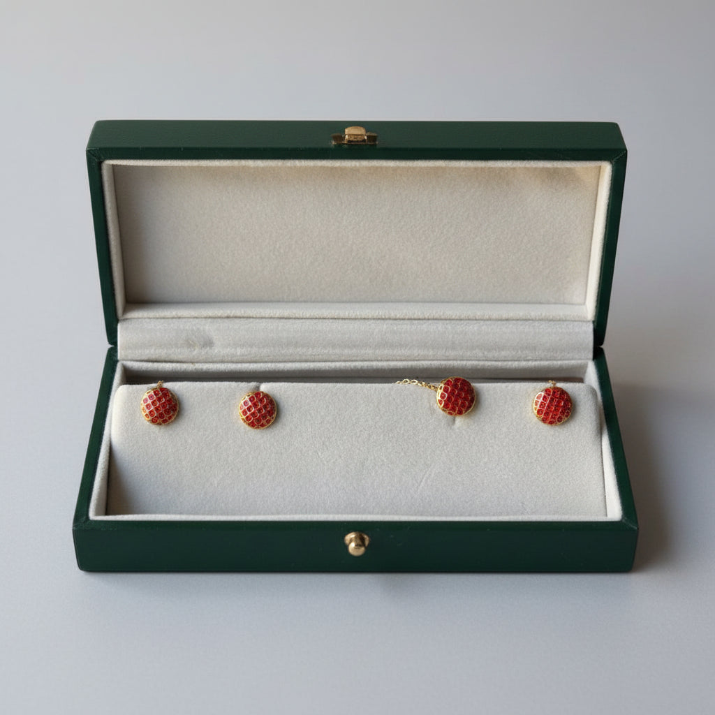 Four red and gold small buttons displayed inside an open jewelry box with a cream-colored velvet insert.