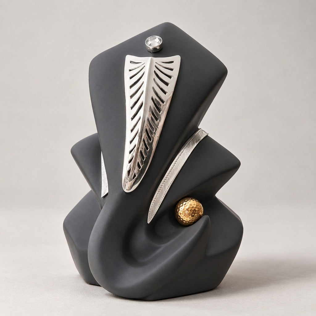 Abstract sculptural figure of Lord Ganesha in matte charcoal gray with silver leaf-like trunk, a small clear faceted gemstone on the forehead, and a textured gold sphere accent on his left.