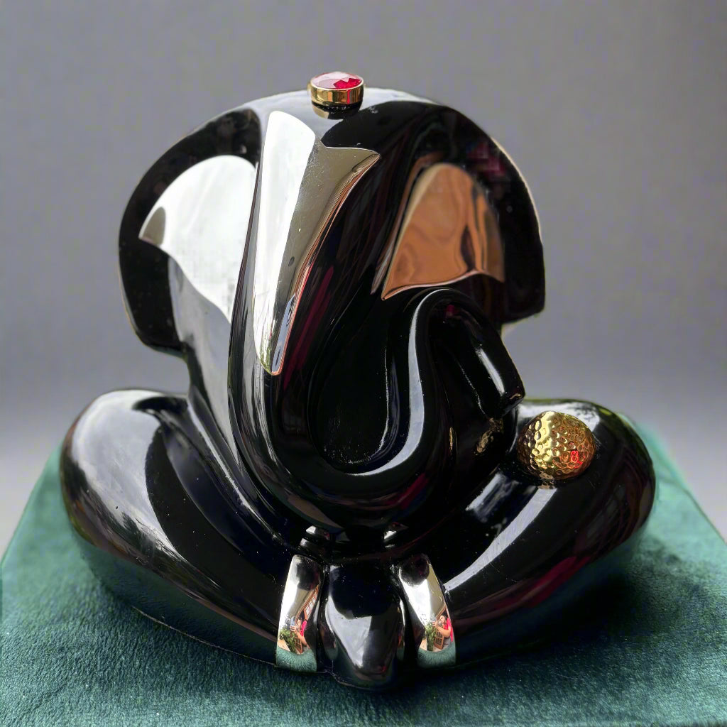 Black and silver decorative object on a green pedestal with blurred greenery in the background