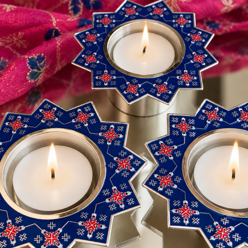 Three star-shaped tealight candle holders with blue, pink, and white floral patterns, each holding a lit white candle, arranged on a mirror base with a patterned fabric in the background.