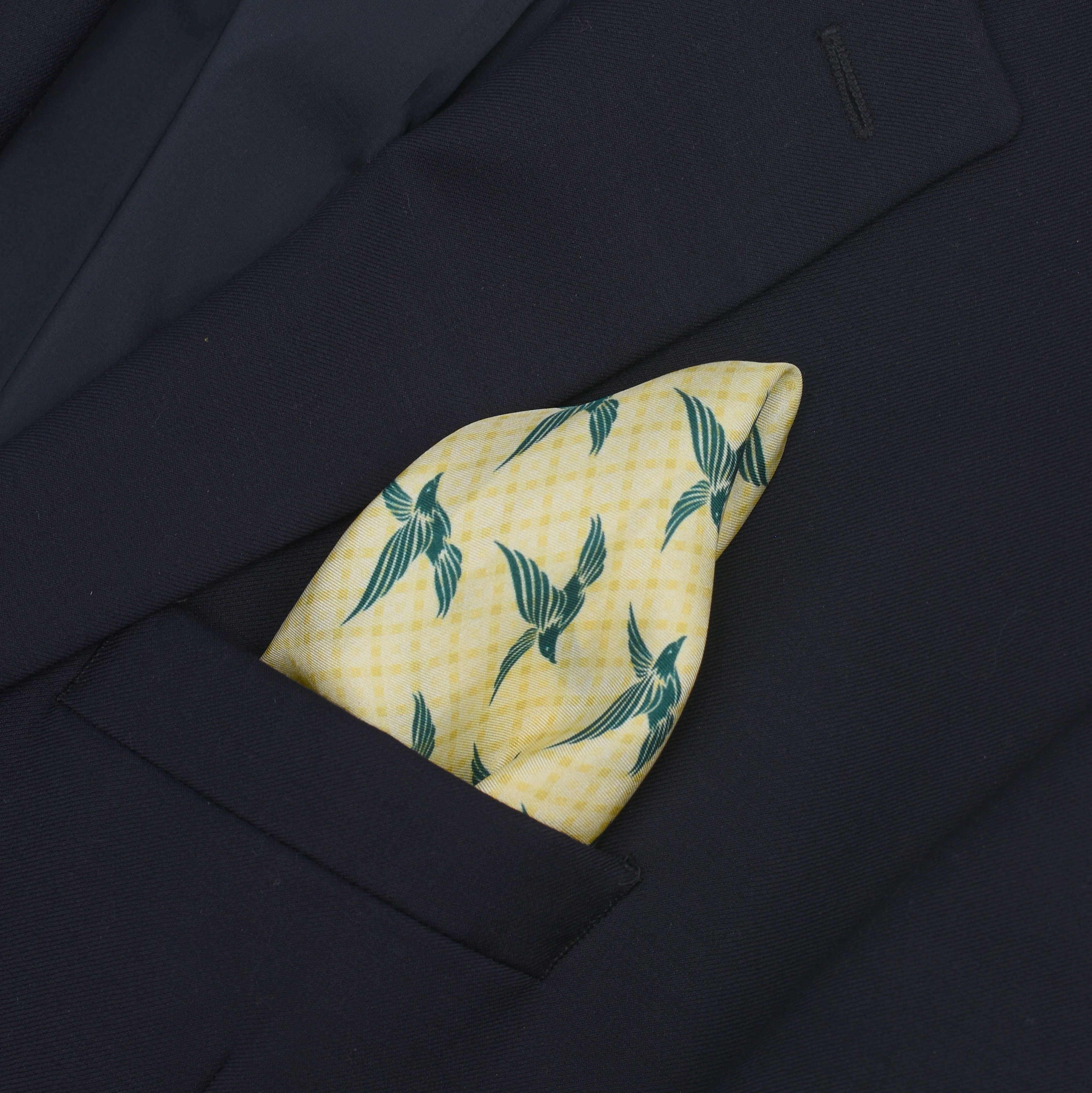 A beige pocket square with green eagle pattern, tucked into the breast pocket of a dark navy suit jacket.